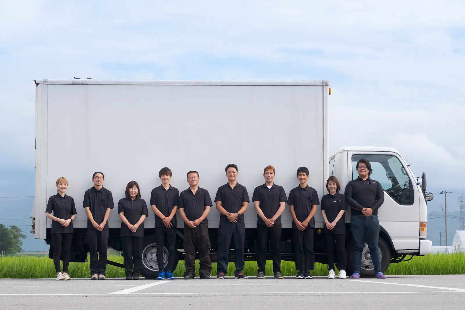 白いトラックの前に一列に並ぶ、黒いユニフォーム姿のAMADOI富山社員の集合写真