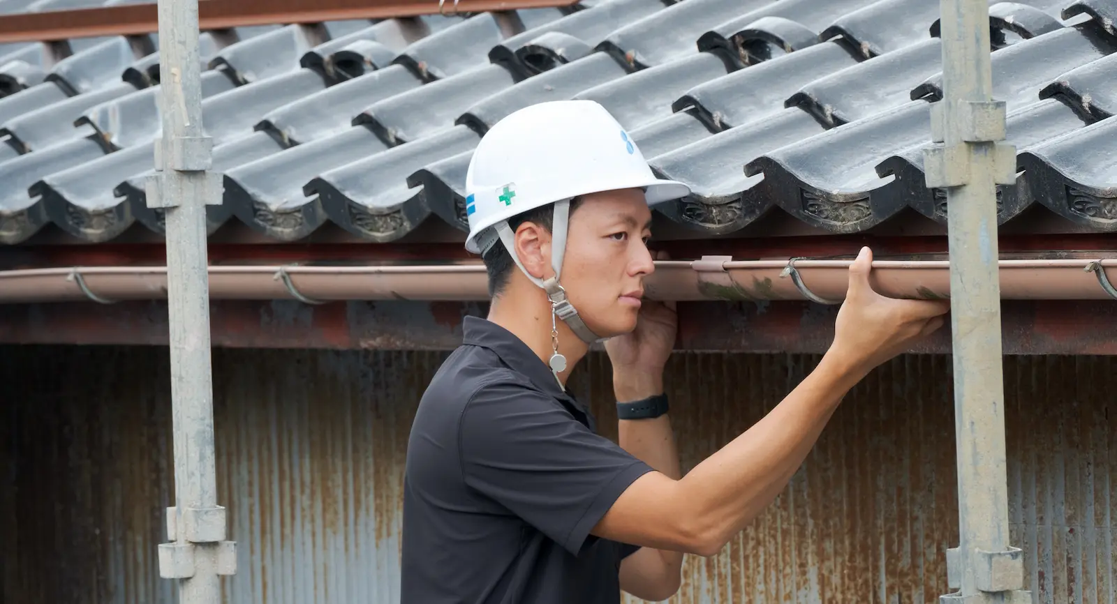 瓦屋根の軒先に設置された雨樋（軒樋）を目視で入念に点検するプロのスタッフ
