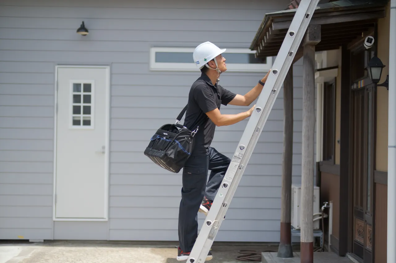 はしごに登って作業を開始しようとする作業員