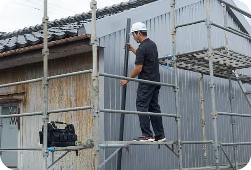 足場の上で雨樋（縦樋）の取り付け作業を行う職人の施工風景