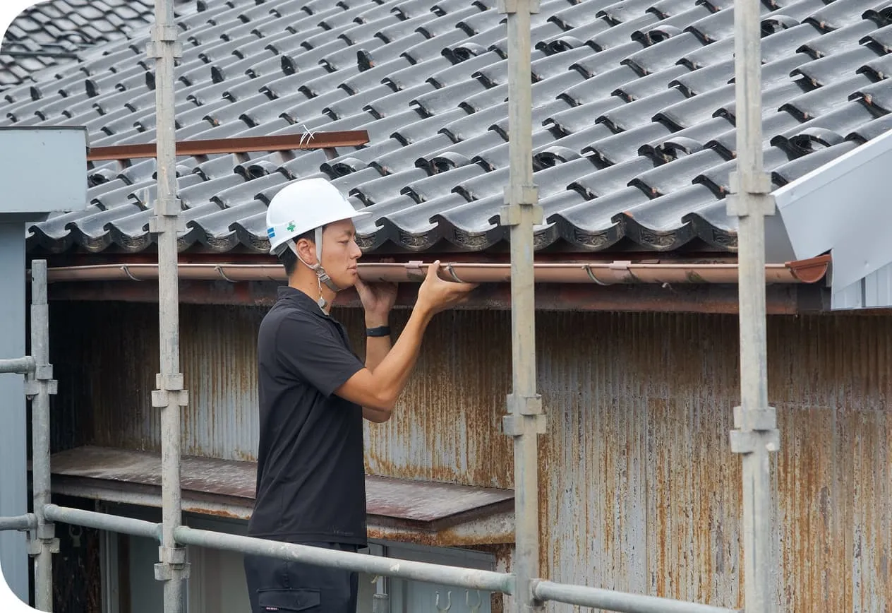 瓦屋根の住宅で、足場を使って軒樋（雨樋）の点検・修理を行う職人の作業風景