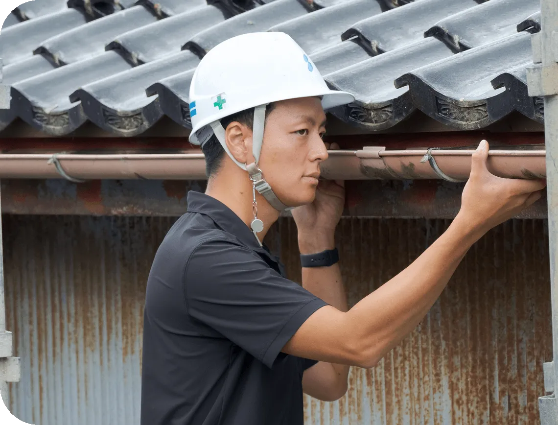 ヘルメットを着用し、真剣な表情で屋根の雨樋（あまどい）を点検する作業員