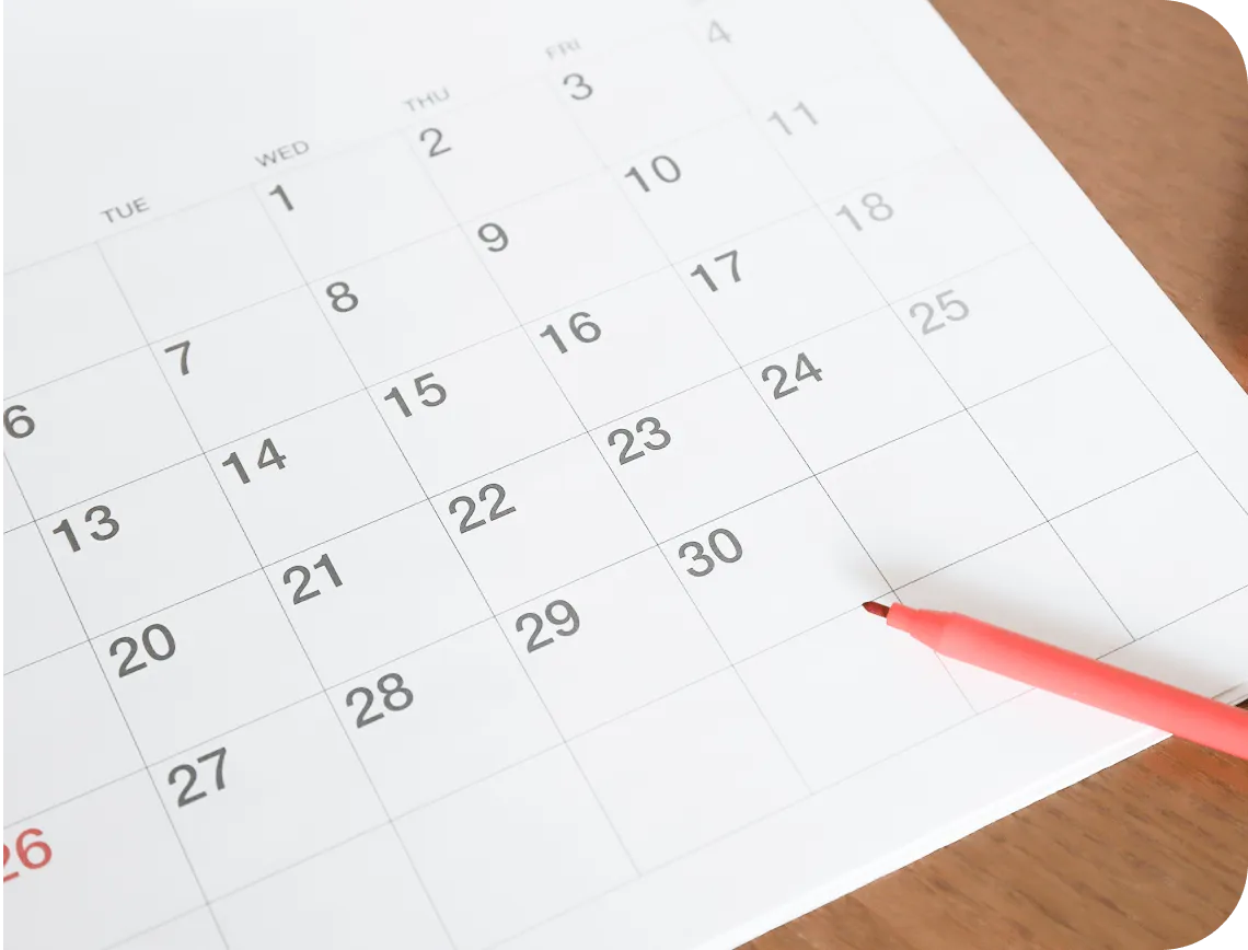 カレンダーの日付を赤いペンで指している様子（スケジュール調整のイメージ）