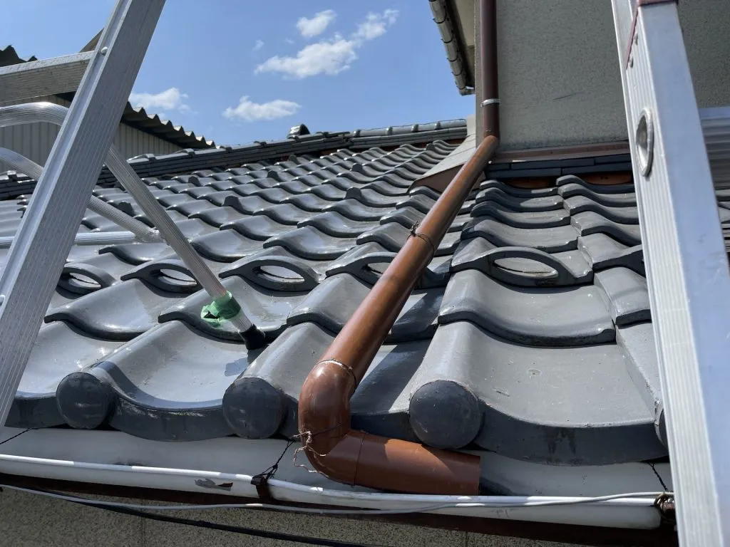 富山県富山市で瓦屋根の上に這わせる新しい茶色の雨樋を設置した施工後の様子