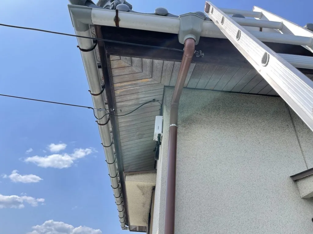 足場を組んで外壁に新しい茶色の竪樋を取り付けている交換工事中の様子