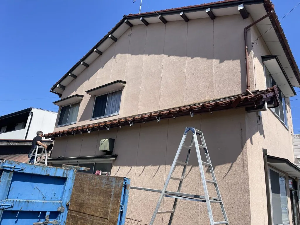 トラックと脚立を使用して高所にある雨樋の交換作業を行っている施工中の様子