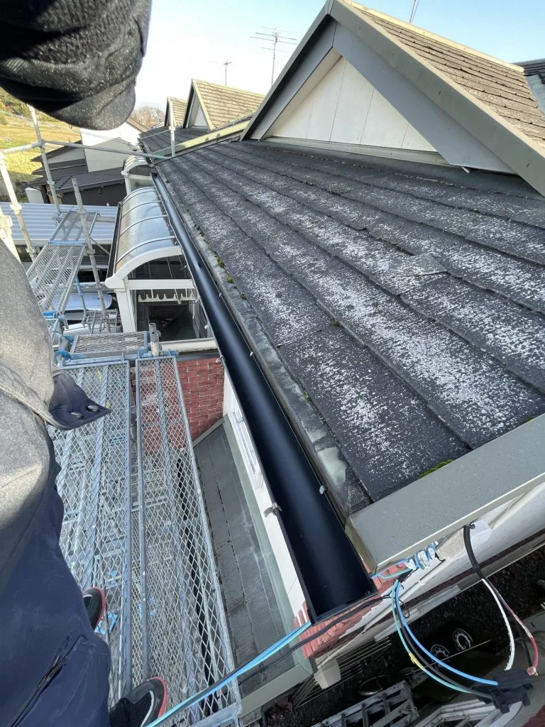 スレート屋根の形状に合わせて新しく黒い雨樋を設置した施工後の様子