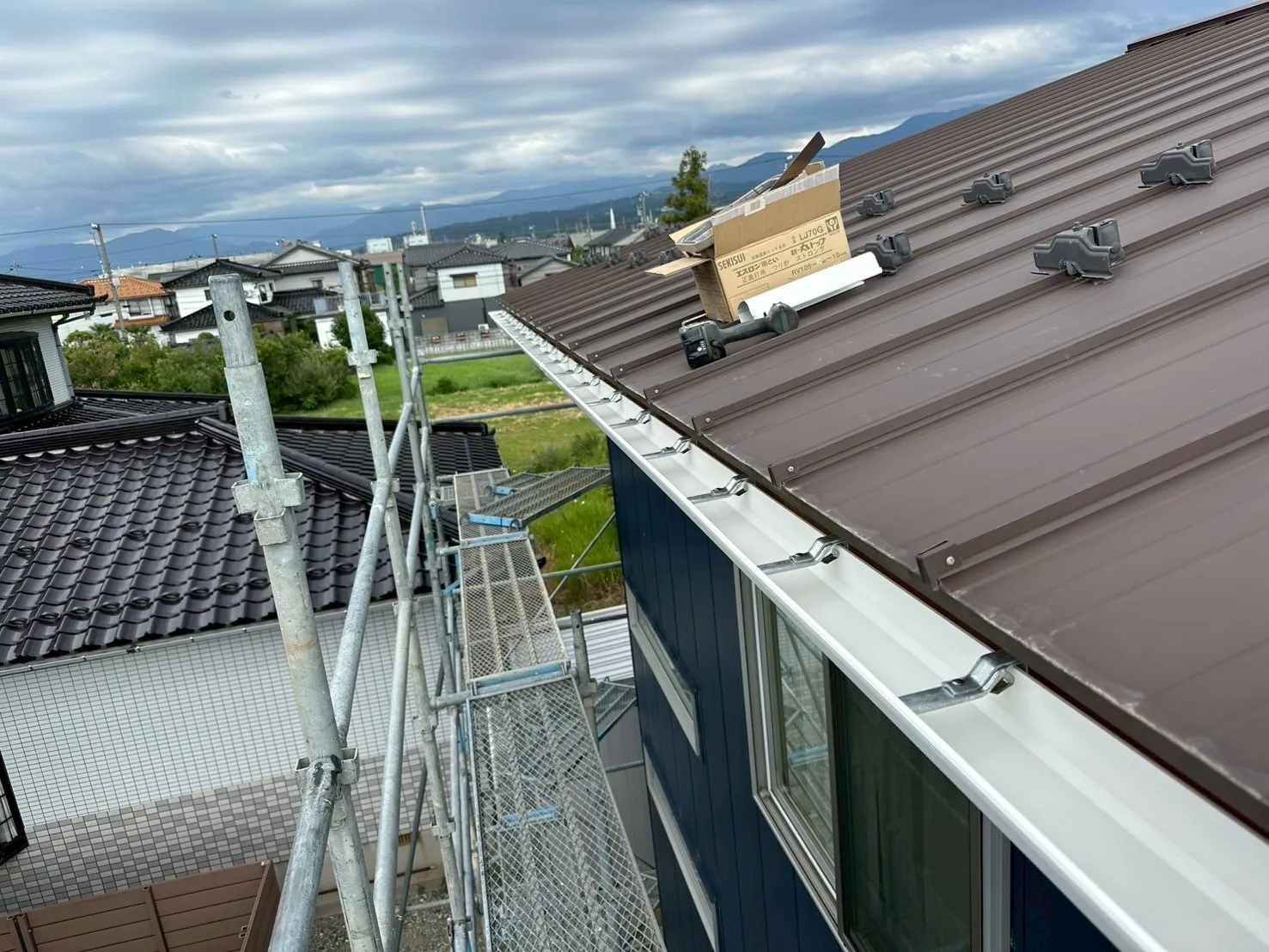 足場を設置して新しい白い雨樋へ取り替えを行っている交換工事の施工風景