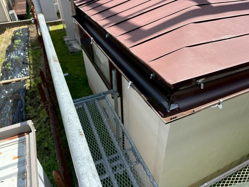 足場を組んで屋根の軒先に新しい茶色の雨樋を取り付けた施工後の様子