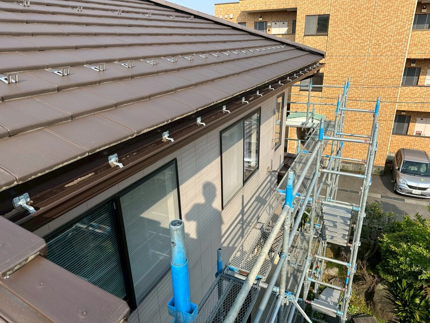 足場を組んで瓦屋根の色に合わせた新しい茶色の雨樋へ交換した施工後の様子