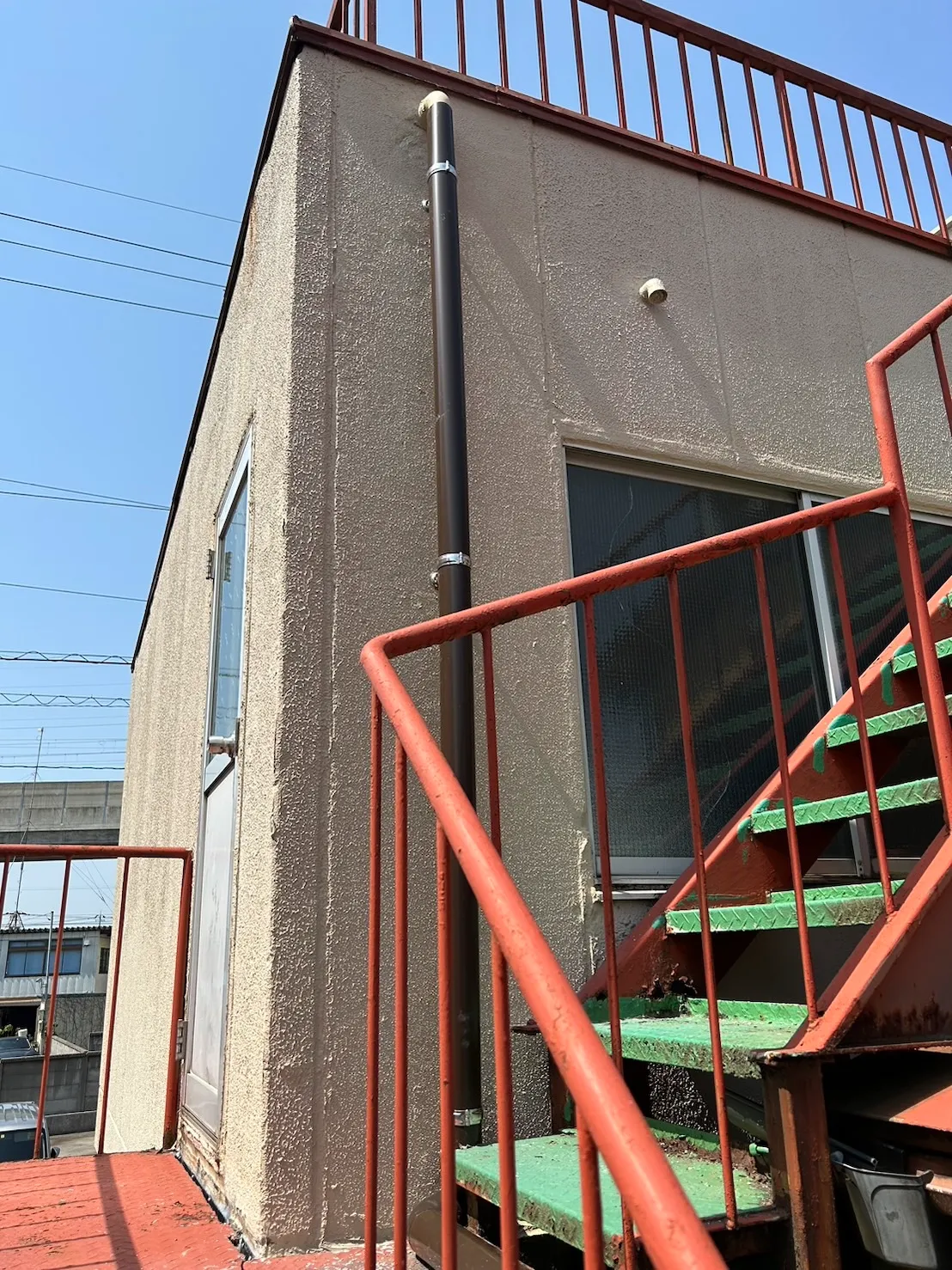 ベージュの外壁に新しい茶色の竪樋を真っ直ぐに固定した施工後の状態