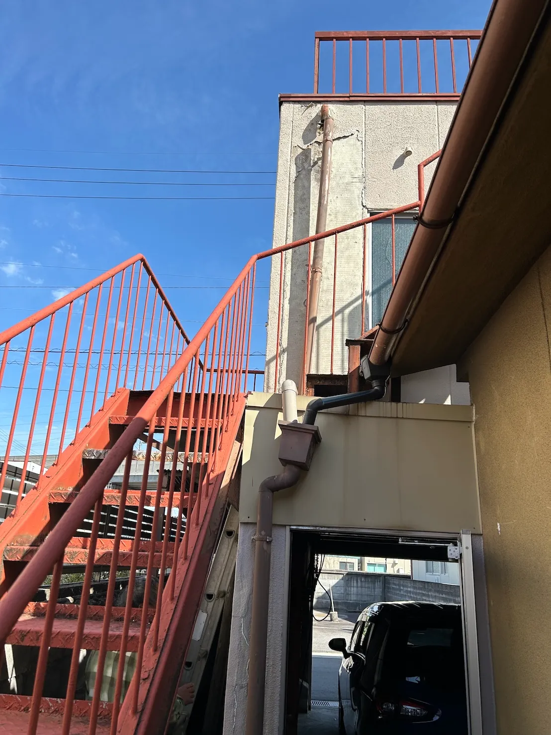 赤い鉄骨階段の脇で折れ曲がり経年劣化していた施工前の古い雨樋の状態