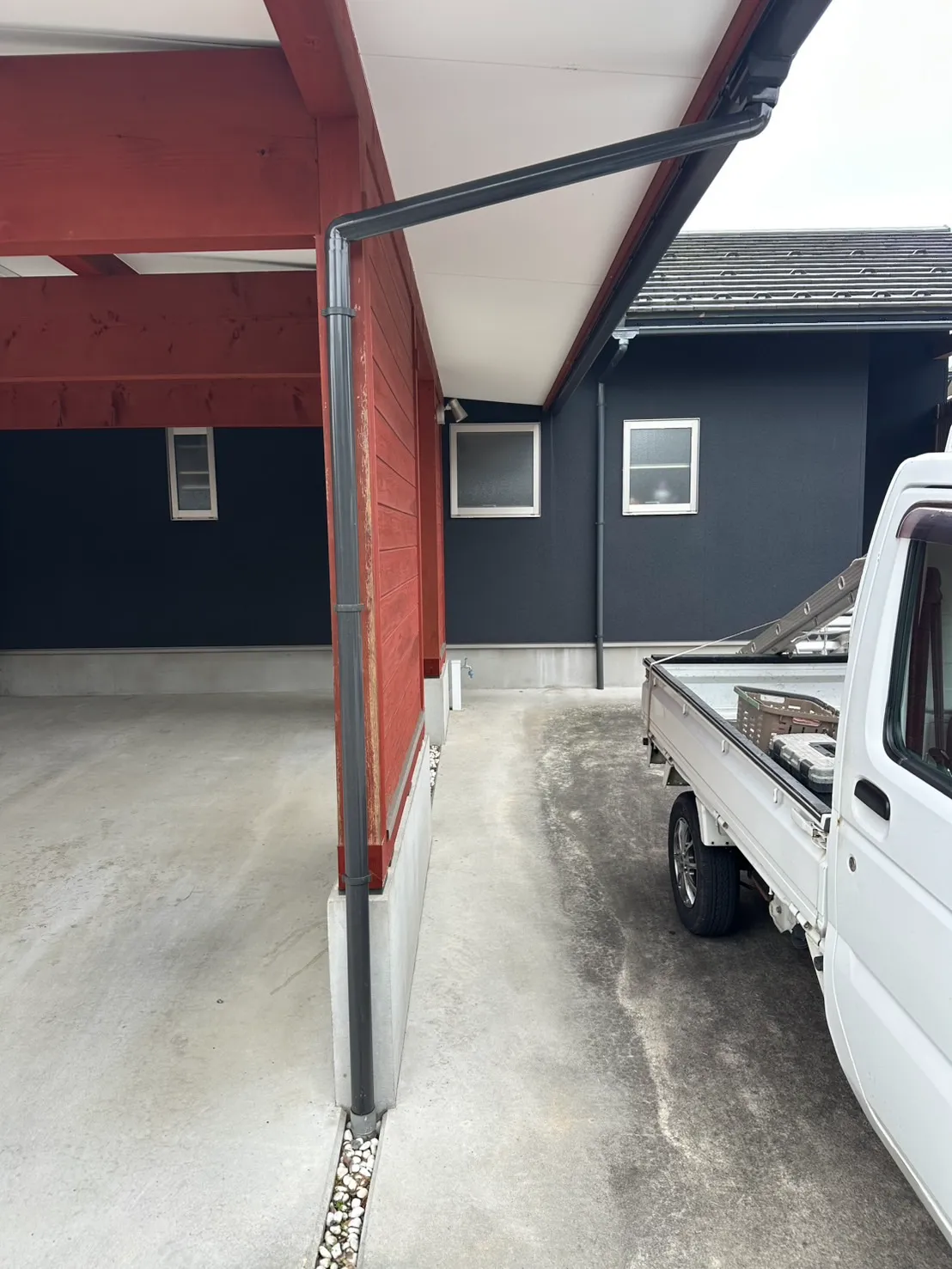 車庫の赤い木製の柱に沿って新しい濃い茶色の竪樋を設置した施工後の様子