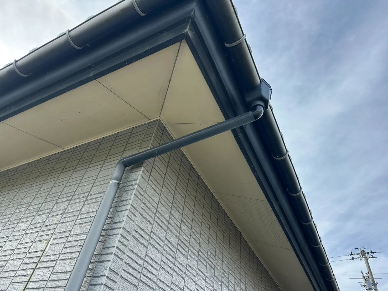 建物のコーナー部分に合わせて角度を調整し新しい黒い雨樋を接続した施工後の様子