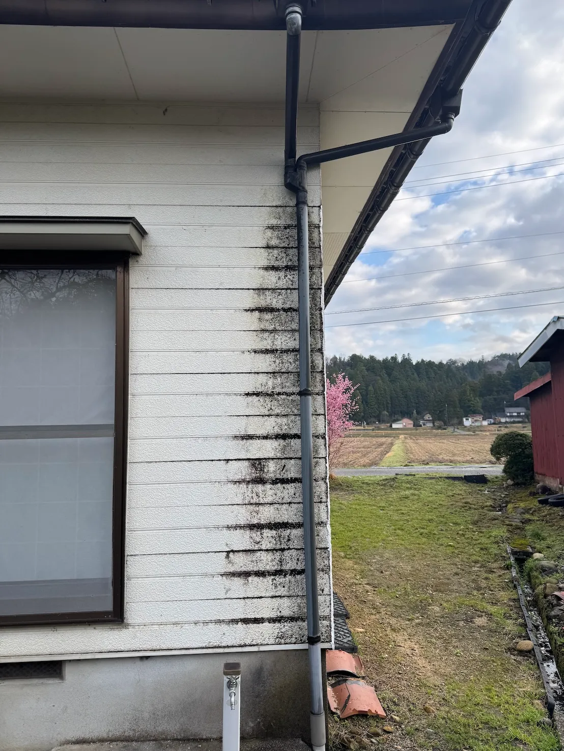 雨樋の不具合により白い外壁に黒い雨だれや汚れが激しく付着している施工前の状態