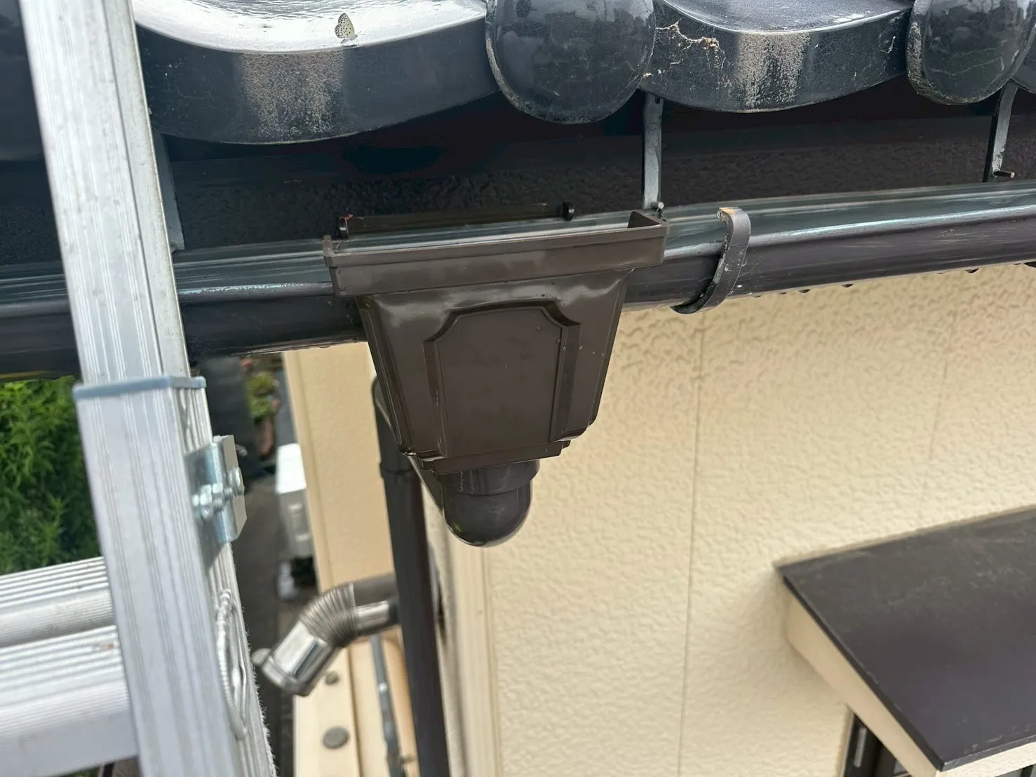 日本瓦の屋根に合わせて新しく交換された光沢のある茶色の雨樋集水器
